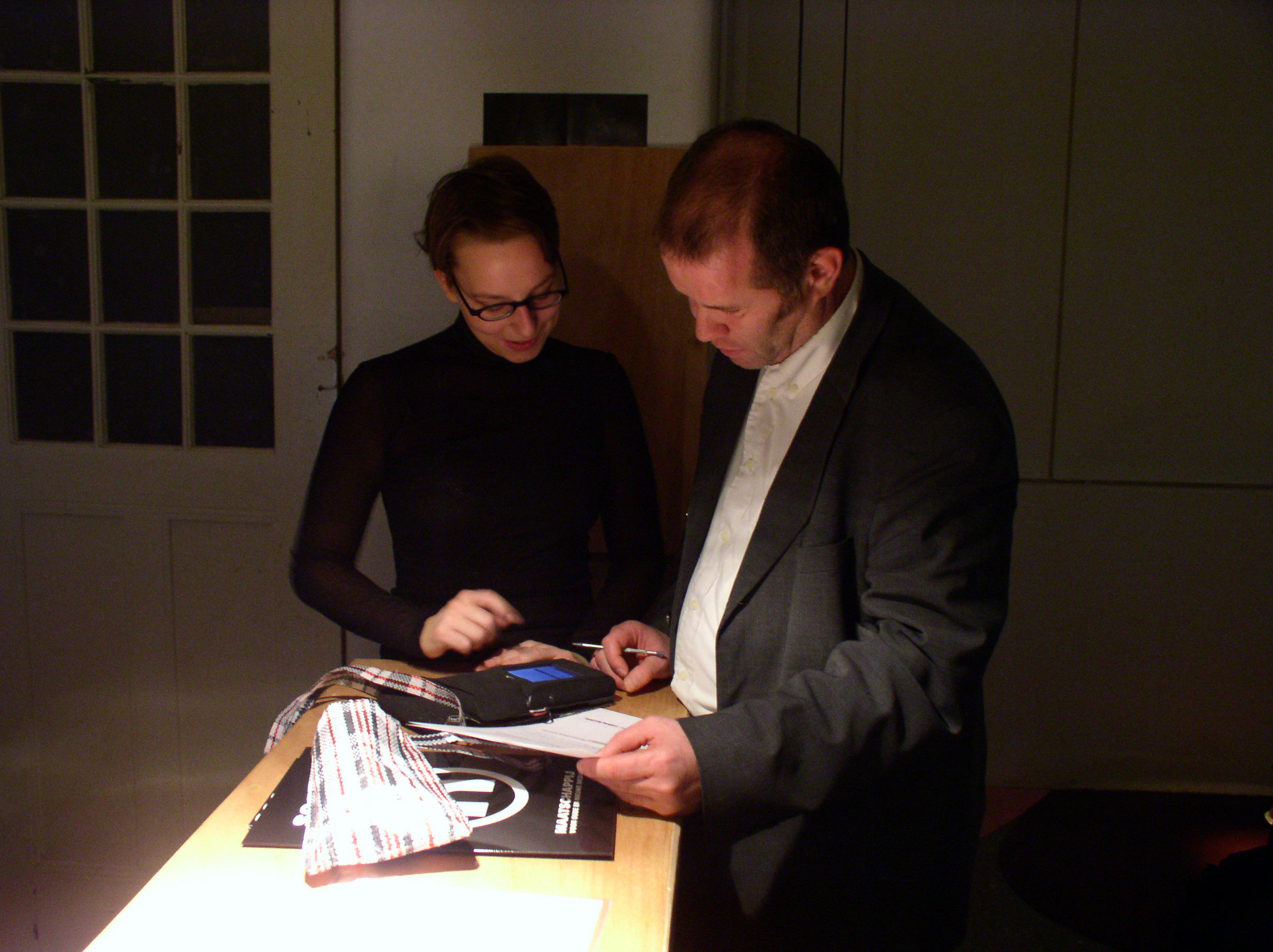 Two people stand at a lit counter examining a PDA tracer and documentation