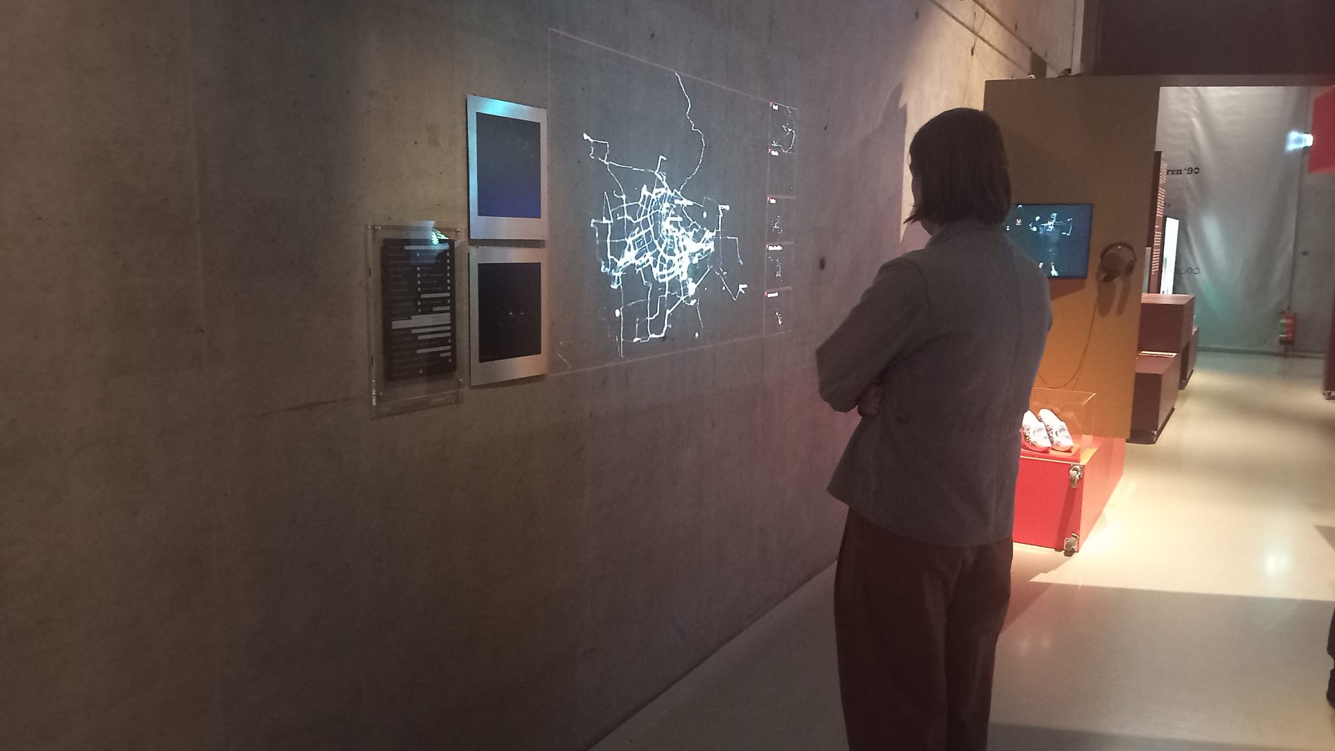 Visitor examines a concrete museum wall with an illuminated GPS route map and smaller prints of individual routes